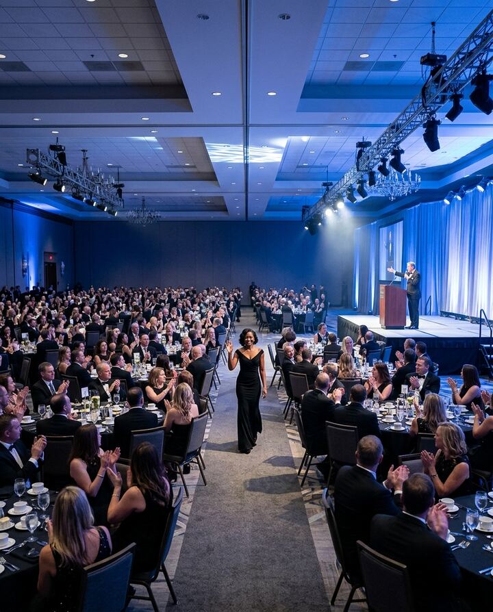 An award winner walking to the stage as guests applaud at a corporate gala