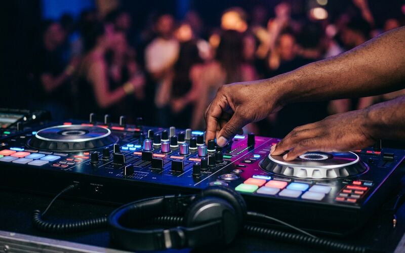 A DJ's hands mixing on a lit-up controller with the dance floor behind